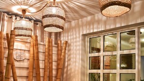 Quarto com decoração em bambu, janela com vários painéis e um banquinho com uma planta.