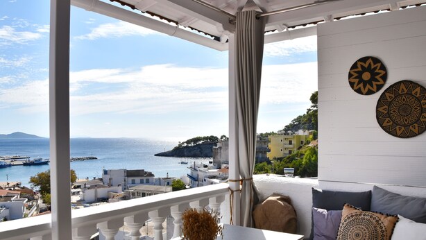 Uma varanda com vista para o mar e edifícios, uma mesa com um vaso e um sofá com almofadas.