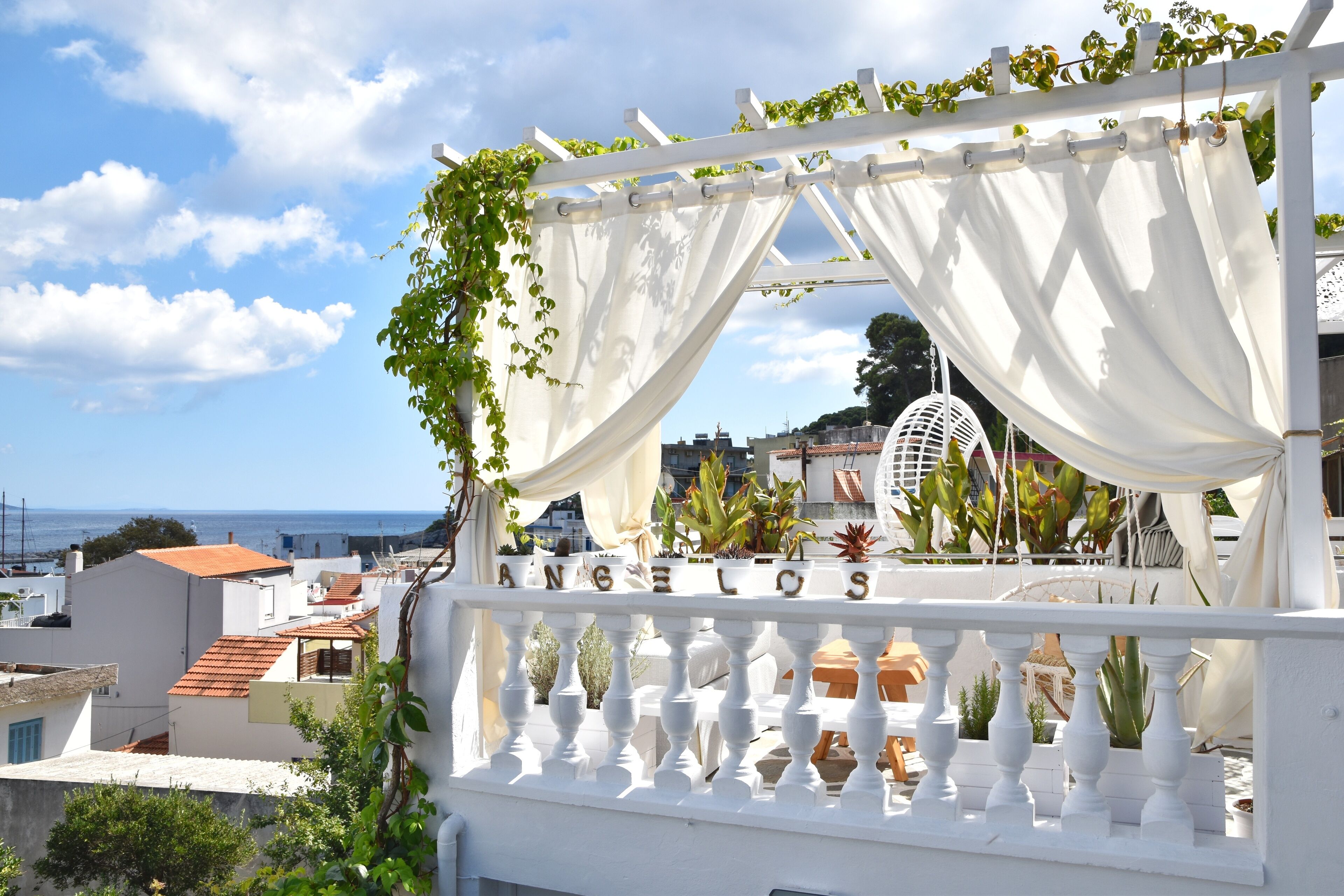 Een wit balkon met een witte leuning, witte gordijnen en de naam 'ANGELOS' in witte letters.