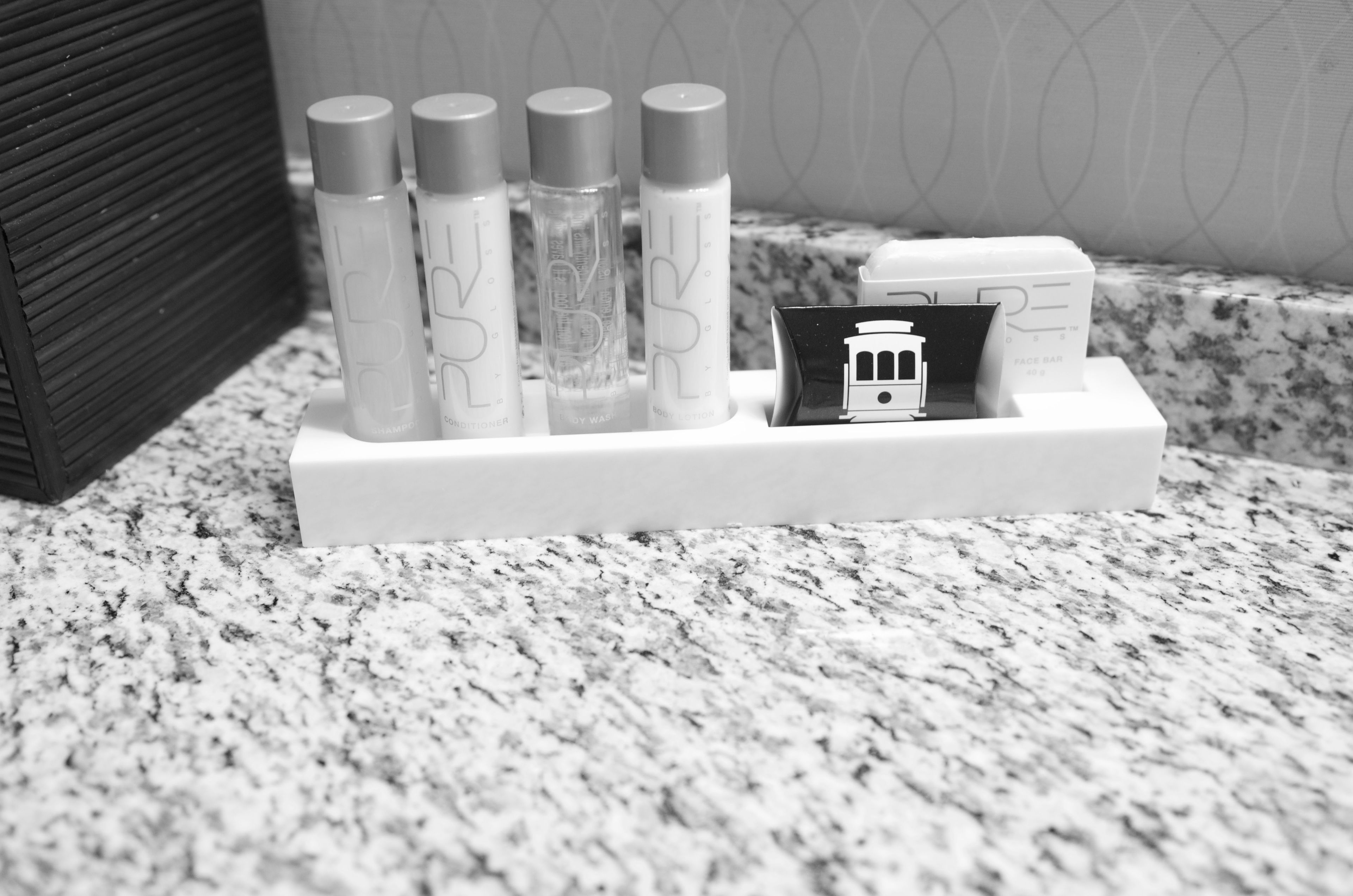A bathroom vanity with a marble countertop, a white soap dispenser holder, and a small black and white photo of a train.