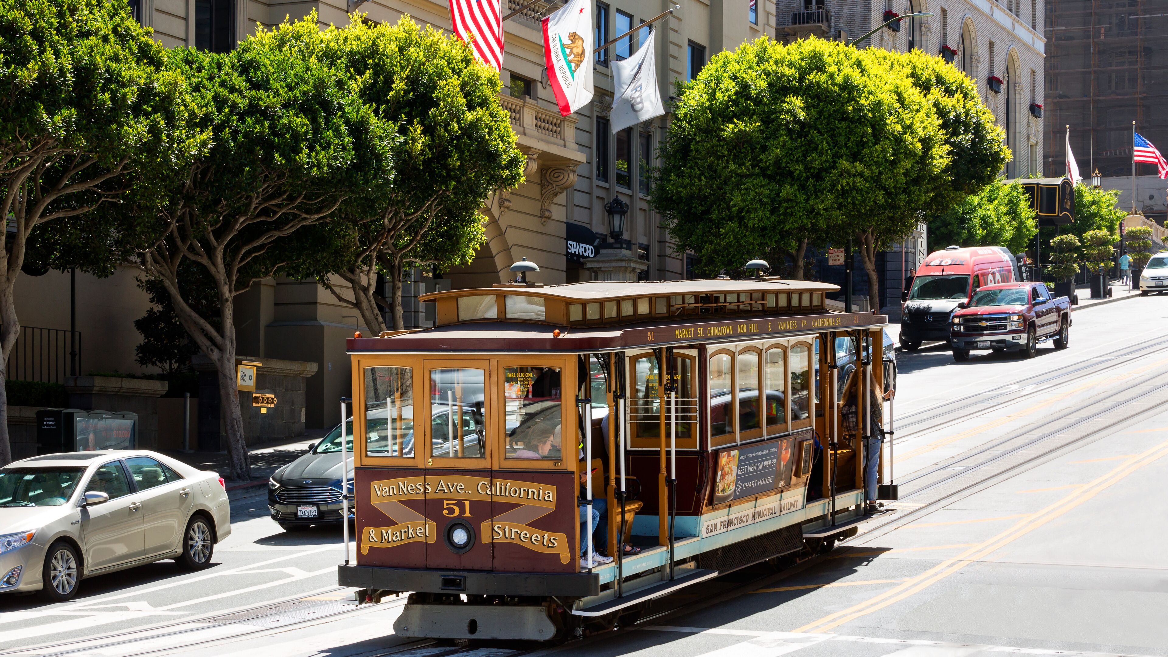 A vintage streetcar on a city street with buildings and flags in the background.