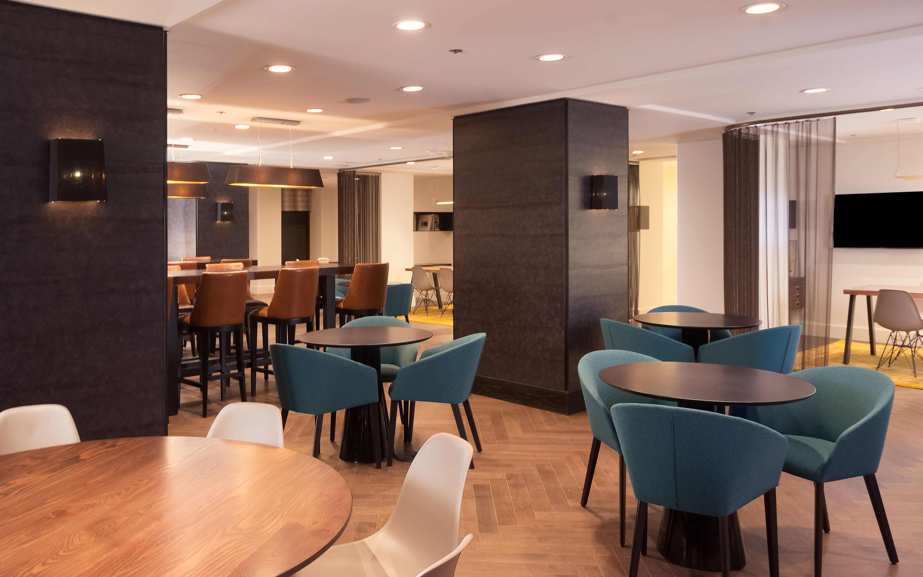 A modern dining area with round tables and chairs, a flat-screen TV, and a large pillar.