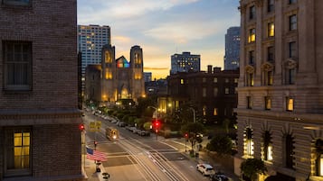 A city street at dusk with historic buildings, a tram, and a clear sky.