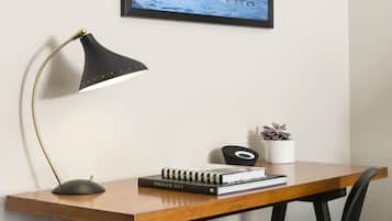A wooden desk with a black chair, a black desk lamp, a framed picture, and a small potted plant.