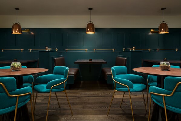 Un interior de restaurante con sillas color turquesa, mesas de madera e iluminación colgante.