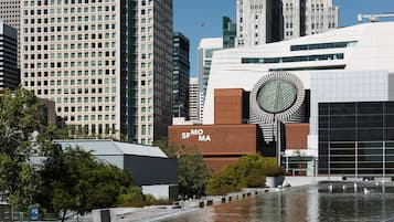 Um edifício moderno com um elemento de design circular marcante, rodeado por um espelho d'água e arranha-céus urbanos.