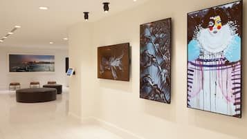 A modern hotel lobby with a minimalist design, featuring a reception desk, seating area, and artwork on the walls.