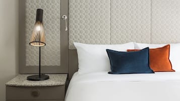 A neatly made bed with white and two colored pillows, a modern lamp on a nightstand, and a textured wall behind the bed.