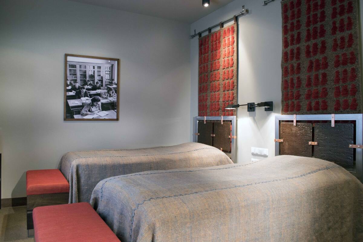 Ein Zimmer mit zwei Betten, einem gerahmten Foto an der Wand und einem roten, gemusterten Vorhang.