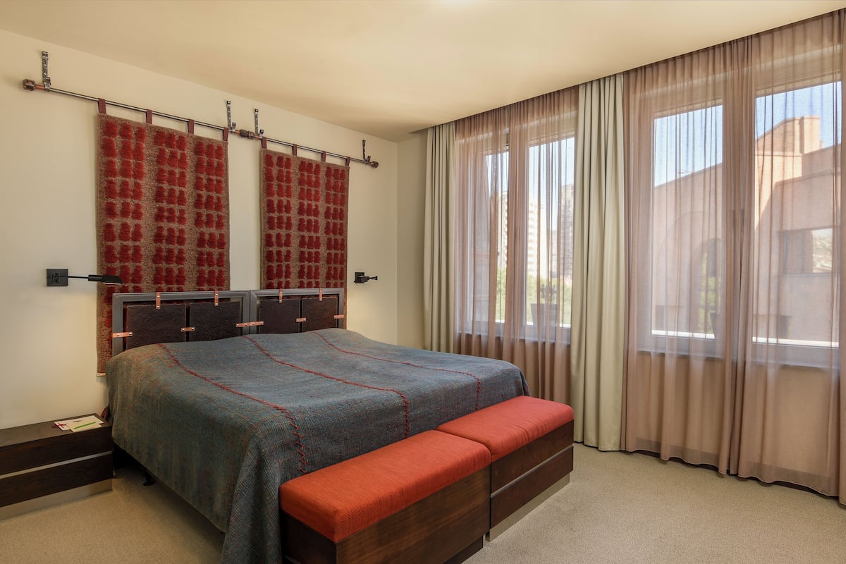 Ein Schlafzimmer mit Bett, Sitzbank, Kleiderschrank und Vorhängen.