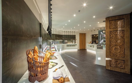 A modern hotel lobby with a buffet area featuring bread and pastries, a counter with various food items, and a decorative wooden panel.