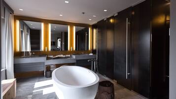 Een moderne badkamer met een vrijstaand ligbad, donkere kastjes en een grote spiegel met ingebouwde verlichting.
