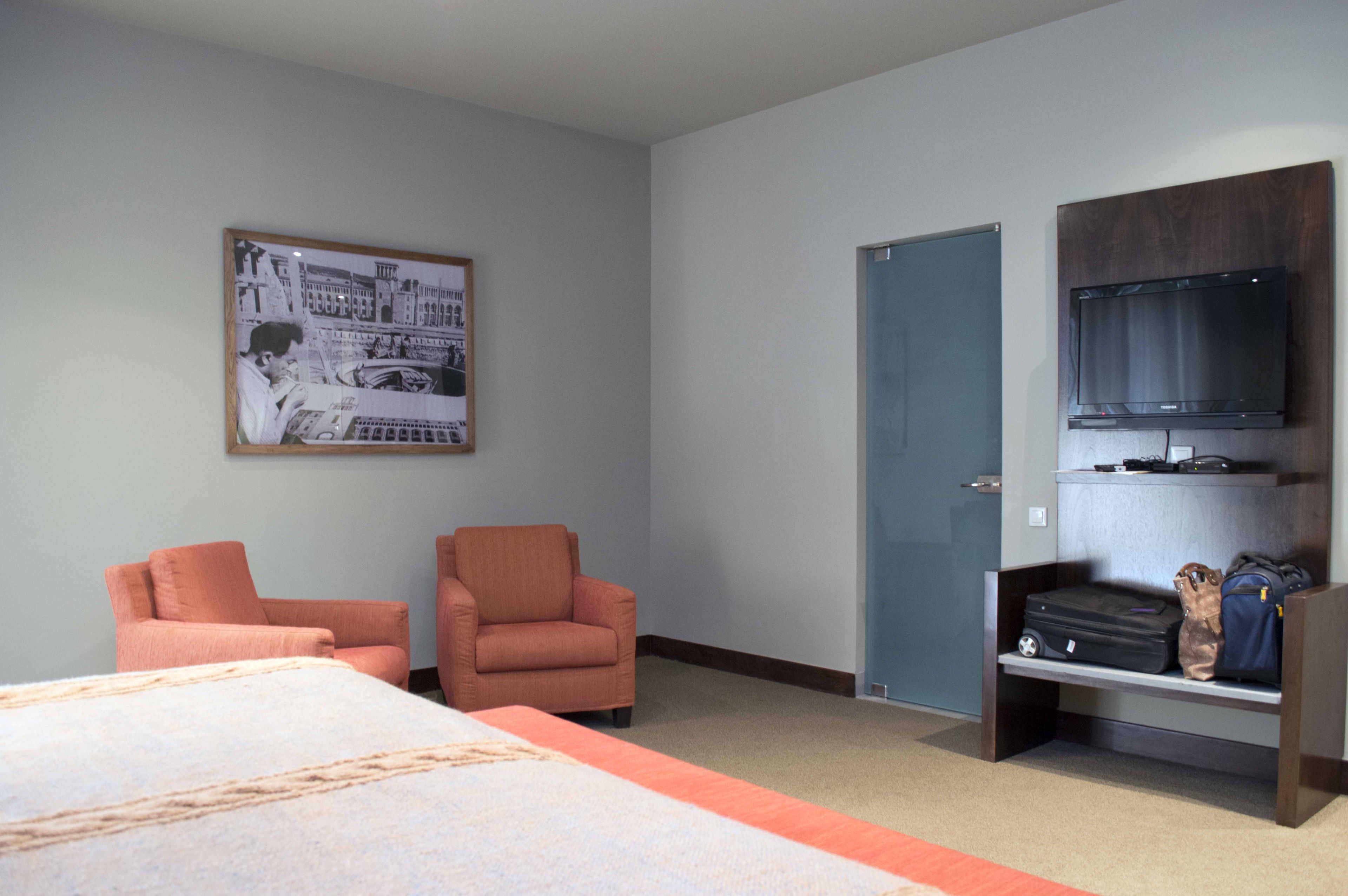 Ein Hotelzimmer mit einem Bett, zwei Sesseln, einem Fernseher und einem Regal mit Gepäck.