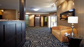 Un hall d’hôtel avec un tapis à motifs, un comptoir d’accueil, un canapé et une lampe.