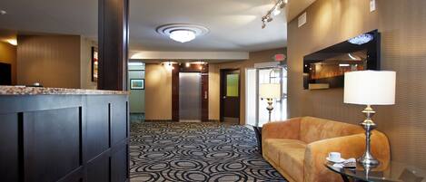 Un hall de hotel con alfombra estampada, una recepción, un sofá y una lámpara.