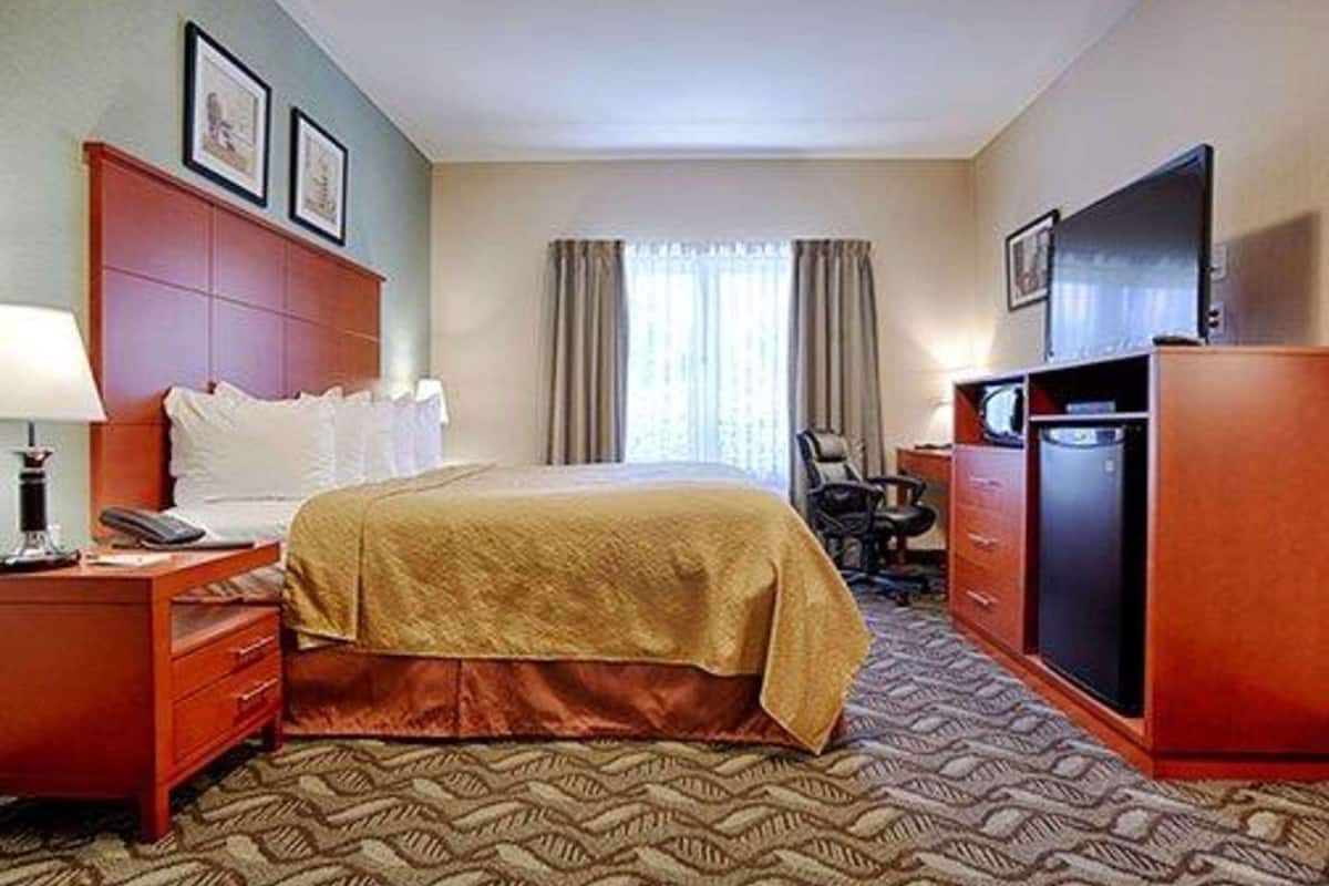 A hotel room with a bed, a desk, a chair, a television, and a wardrobe.