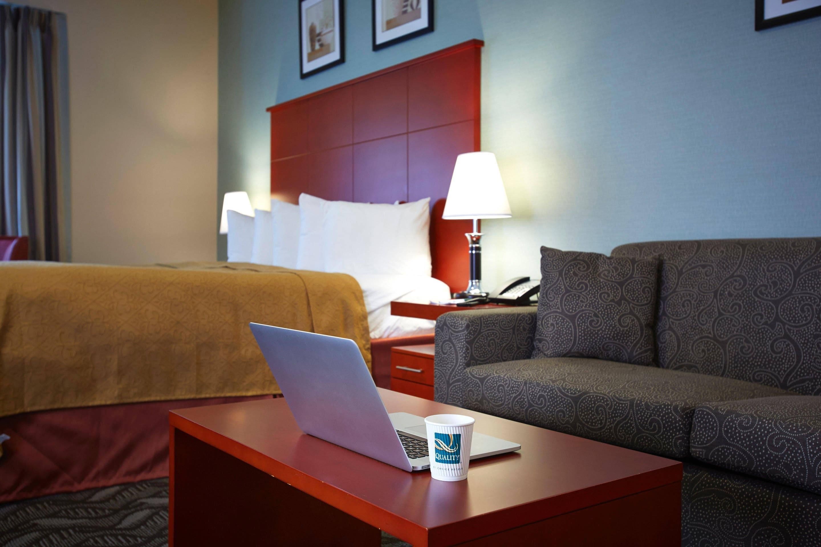 Ein Hotelzimmer mit einem Bett, einer Couch, einem Schreibtisch mit einem Laptop und einer Tasse.