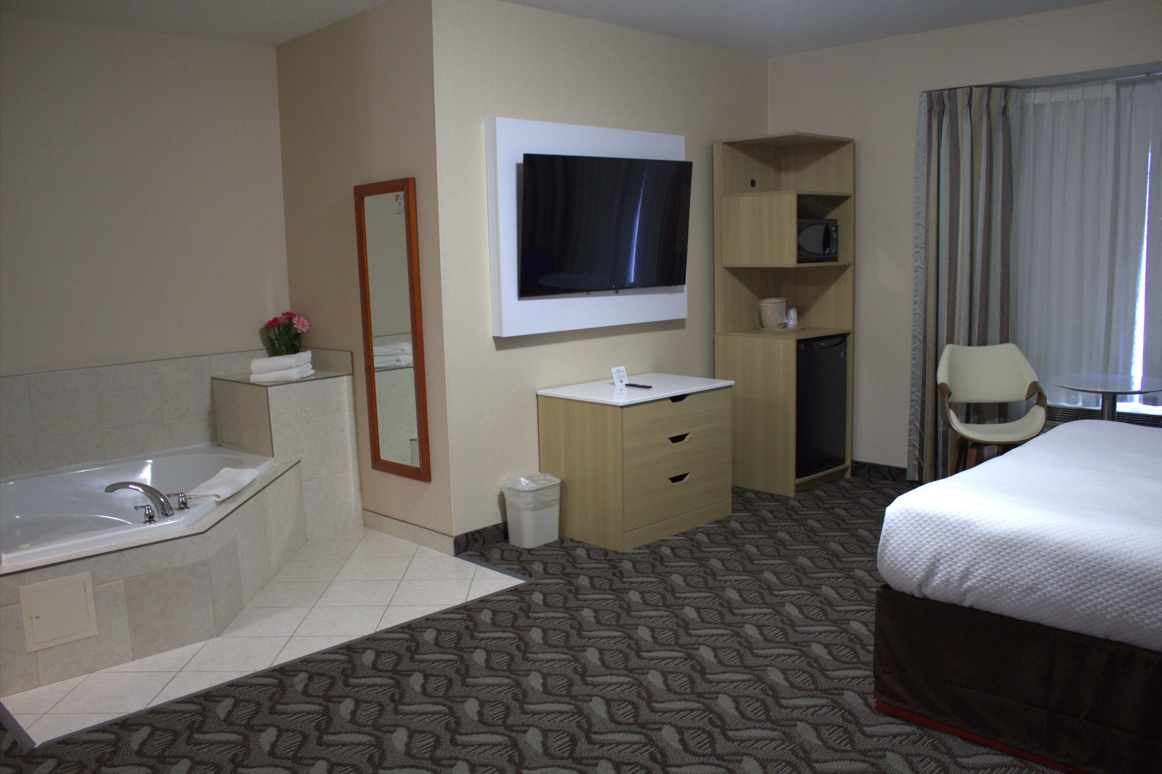 A hotel room with a large bed, a bathroom with a bathtub, a TV mounted on the wall, and a desk with a chair.