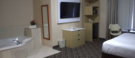 A hotel room with a large bed, a bathroom with a bathtub, a TV mounted on the wall, and a desk with a chair.