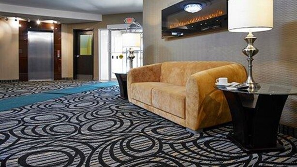 Un hall d’hôtel avec un tapis à motifs, un canapé, une table avec une lampe et une cheminée fixée au mur.