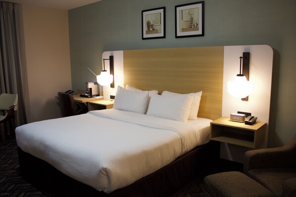 A hotel room with a large bed, two bedside tables with lamps, a chair, and a desk with a telephone. - Quality Inn Southampton (Saugeen Shores)