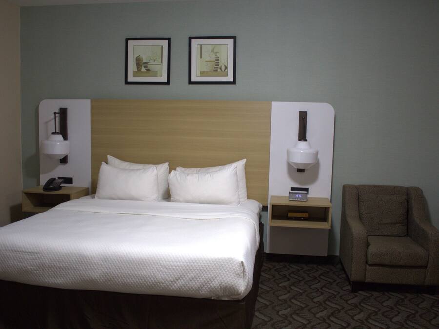 A hotel room with a bed, two bedside tables, a chair, and two framed pictures on the wall.