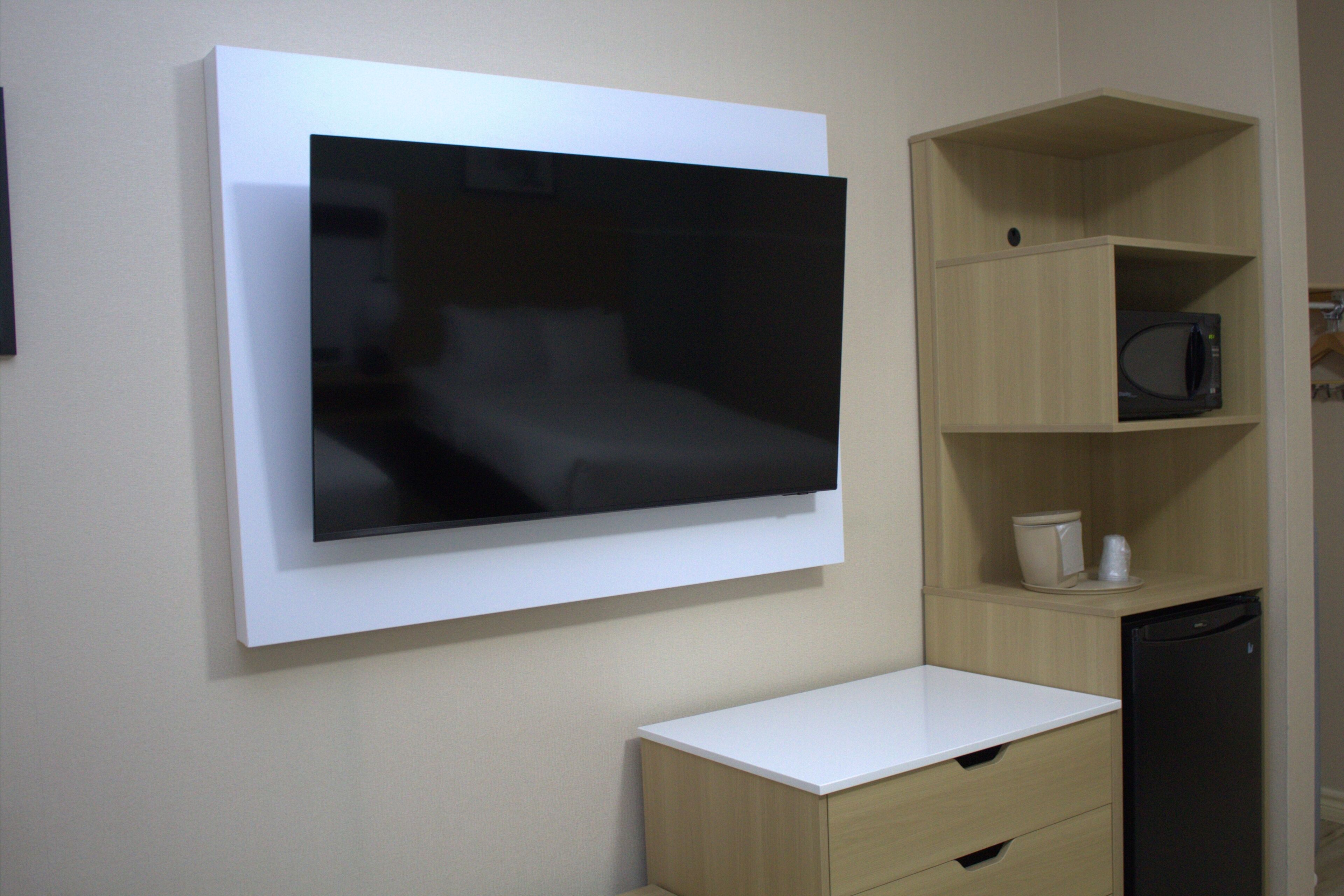 Una habitación moderna con televisión de pantalla plana en la pared, un escritorio blanco, microondas y lavavajillas.