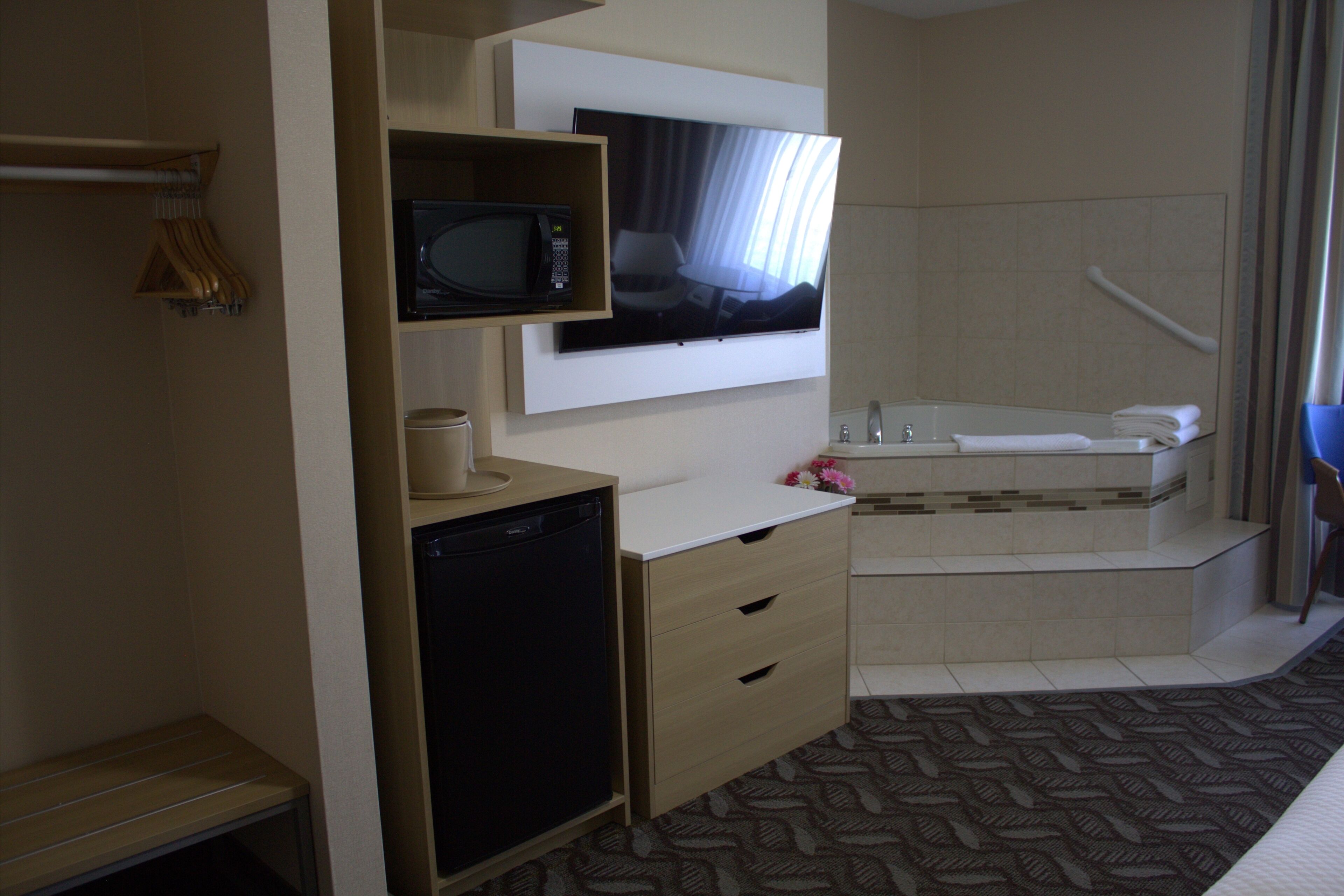 Habitación de hotel con televisión, microondas, refrigerador pequeño y bañera.