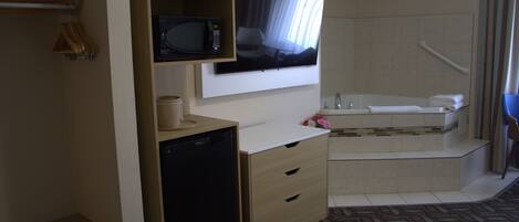 Habitación de hotel con televisión, microondas, refrigerador pequeño y bañera.