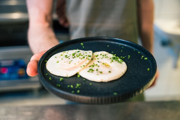 A person holding a black plate with two white, round food items garnished with green herbs. - Hotel No13 (Bergen)
