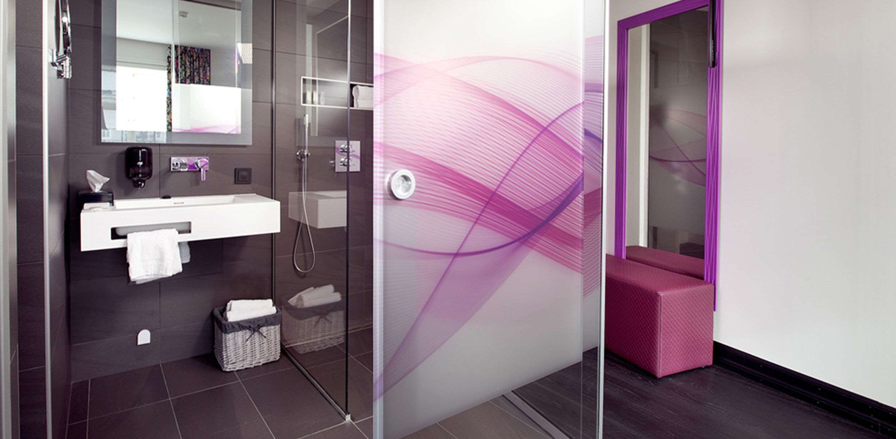 Un baño moderno con cabina de ducha de vidrio, un lavabo blanco y una pared de acento morada.