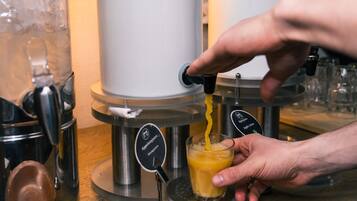 A person pouring orange juice from a dispenser into a glass.