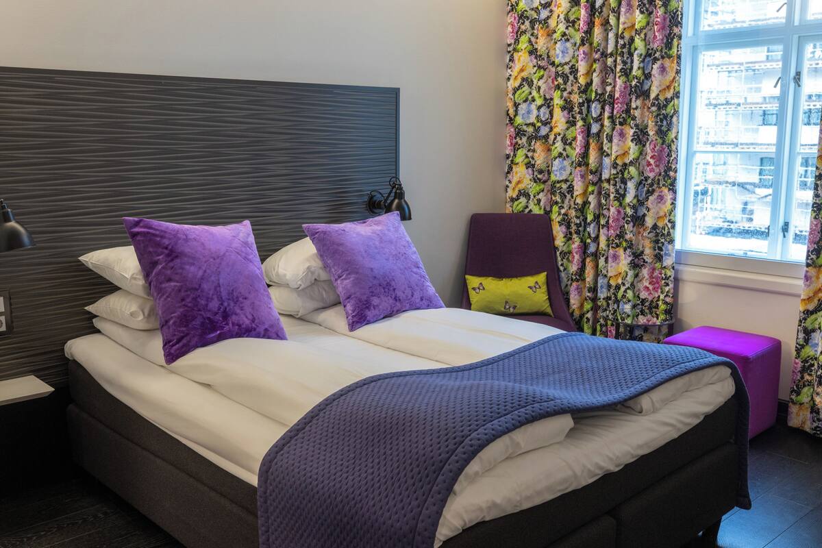 A double bed with white and purple bedding, a dark headboard, and a purple blanket.