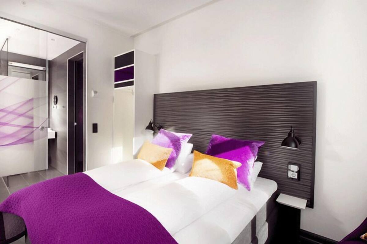A modern bedroom with a large bed, a walk-in closet, and a glass partition.