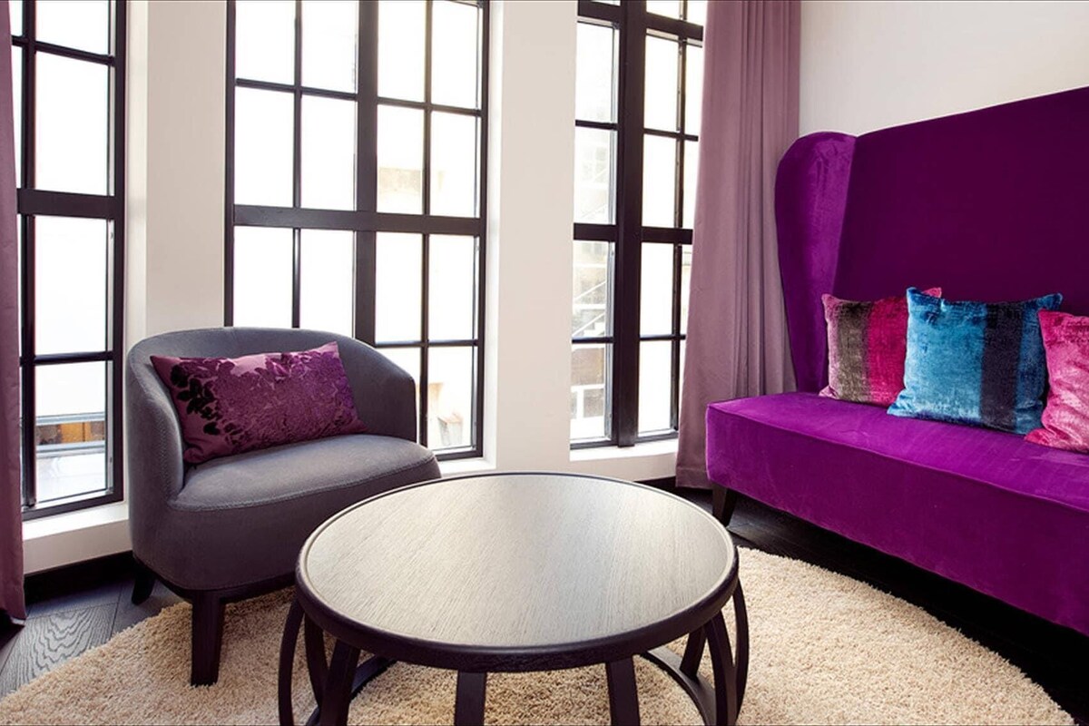 Un salon moderne avec un canapé violet, un fauteuil gris et une table basse ronde.