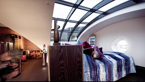 A modern, curved room with a skylight, a bed with a striped blanket, a round window, and a unique wall design.