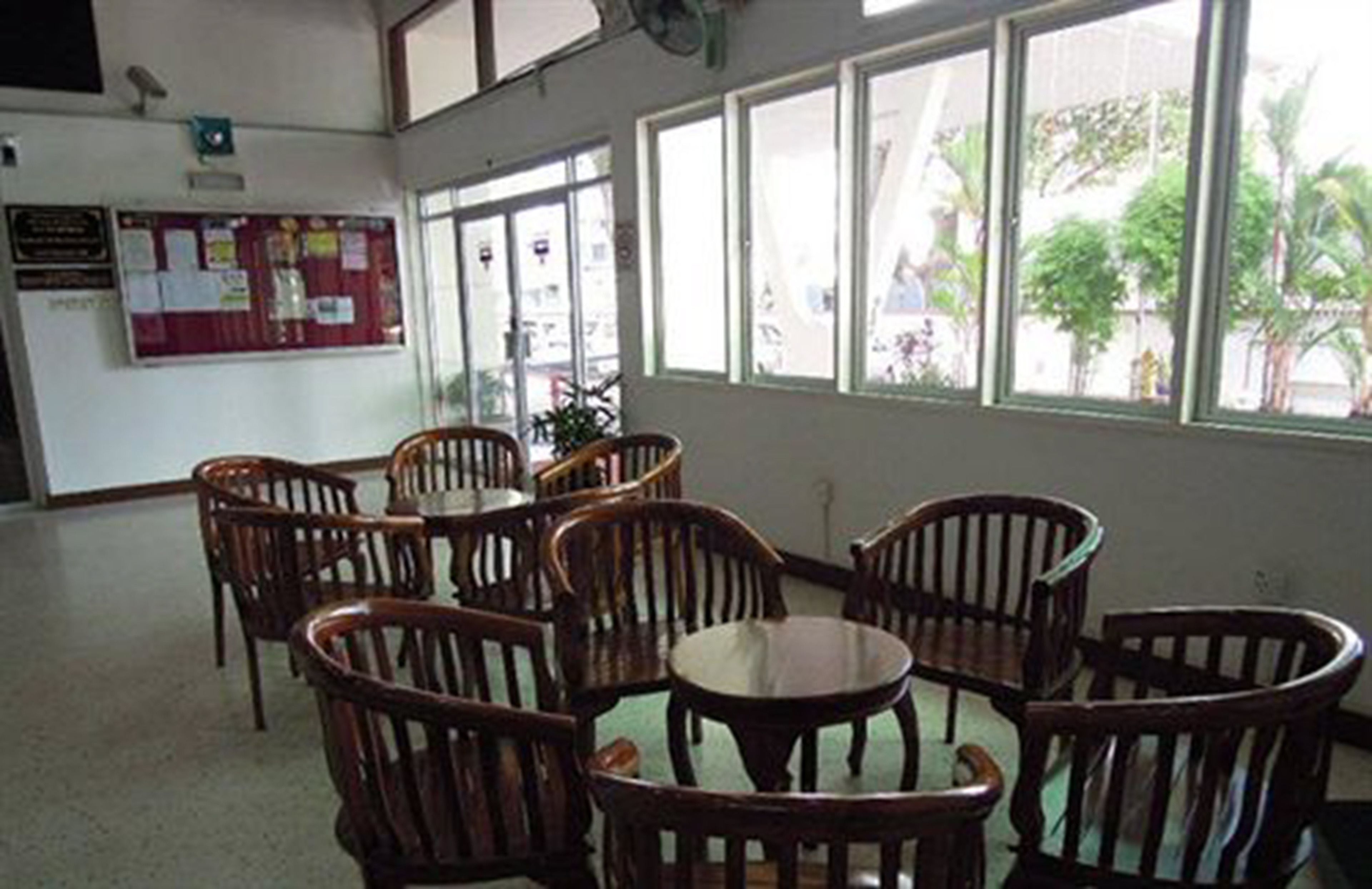 A room with wooden chairs and a table, large windows with a view of greenery outside, and a bulletin board on the wall.