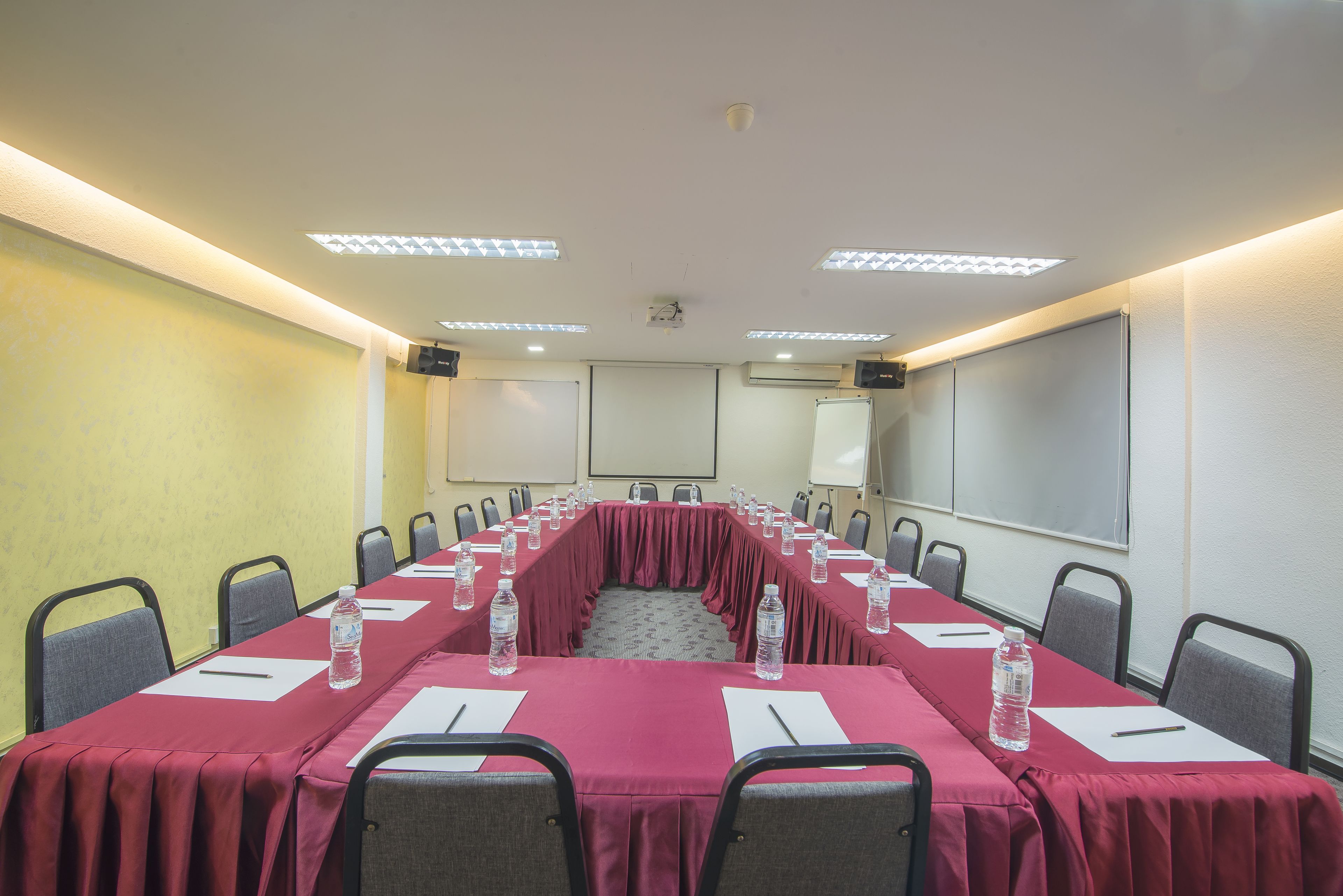 Un salón de conferencias con una mesa larga, sillas, botellas de agua y una pantalla de proyector.