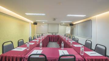Un salón de conferencias con una mesa larga, sillas, botellas de agua y una pantalla de proyector.