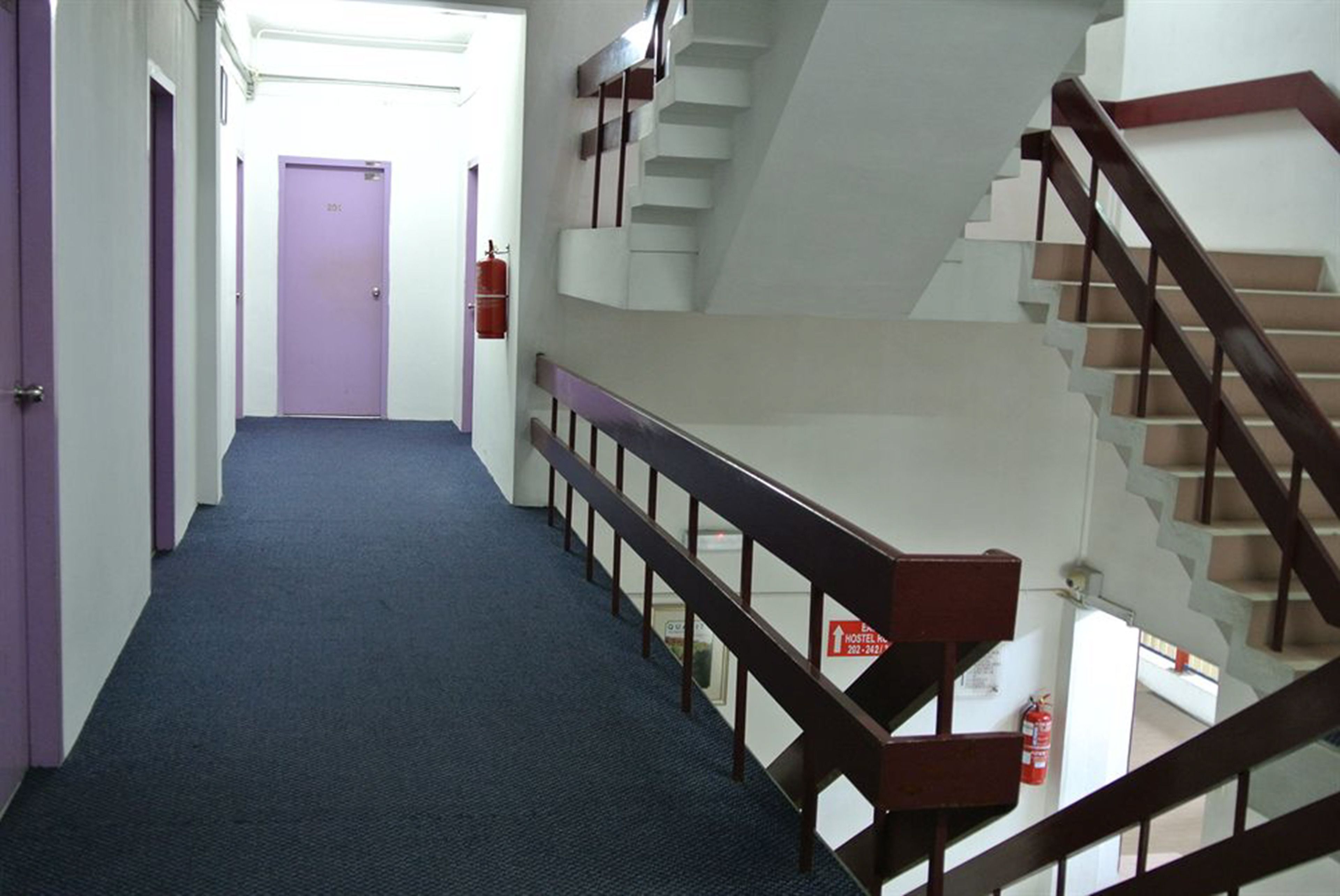 A hotel corridor with purple doors, a blue carpet, and a staircase with wooden railings.