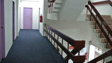 A hotel corridor with purple doors, a blue carpet, and a staircase with wooden railings.