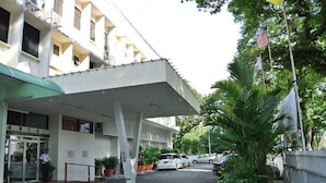 A hotel entrance with a covered walkway, potted plants, and parked cars.