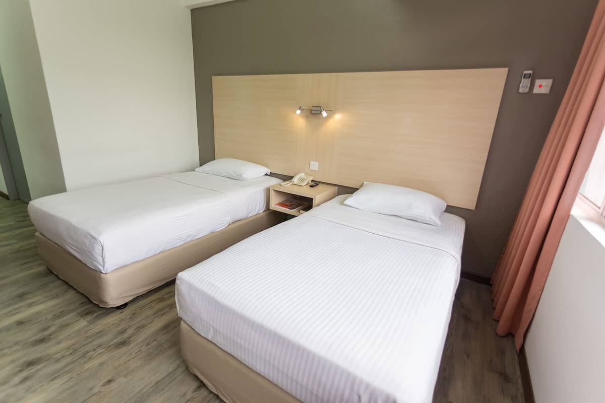A hotel room with two single beds, a bedside table with a phone, and a wall-mounted light fixture.