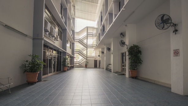 A spacious indoor corridor with tiled floors, potted plants, and multiple fans on the walls.