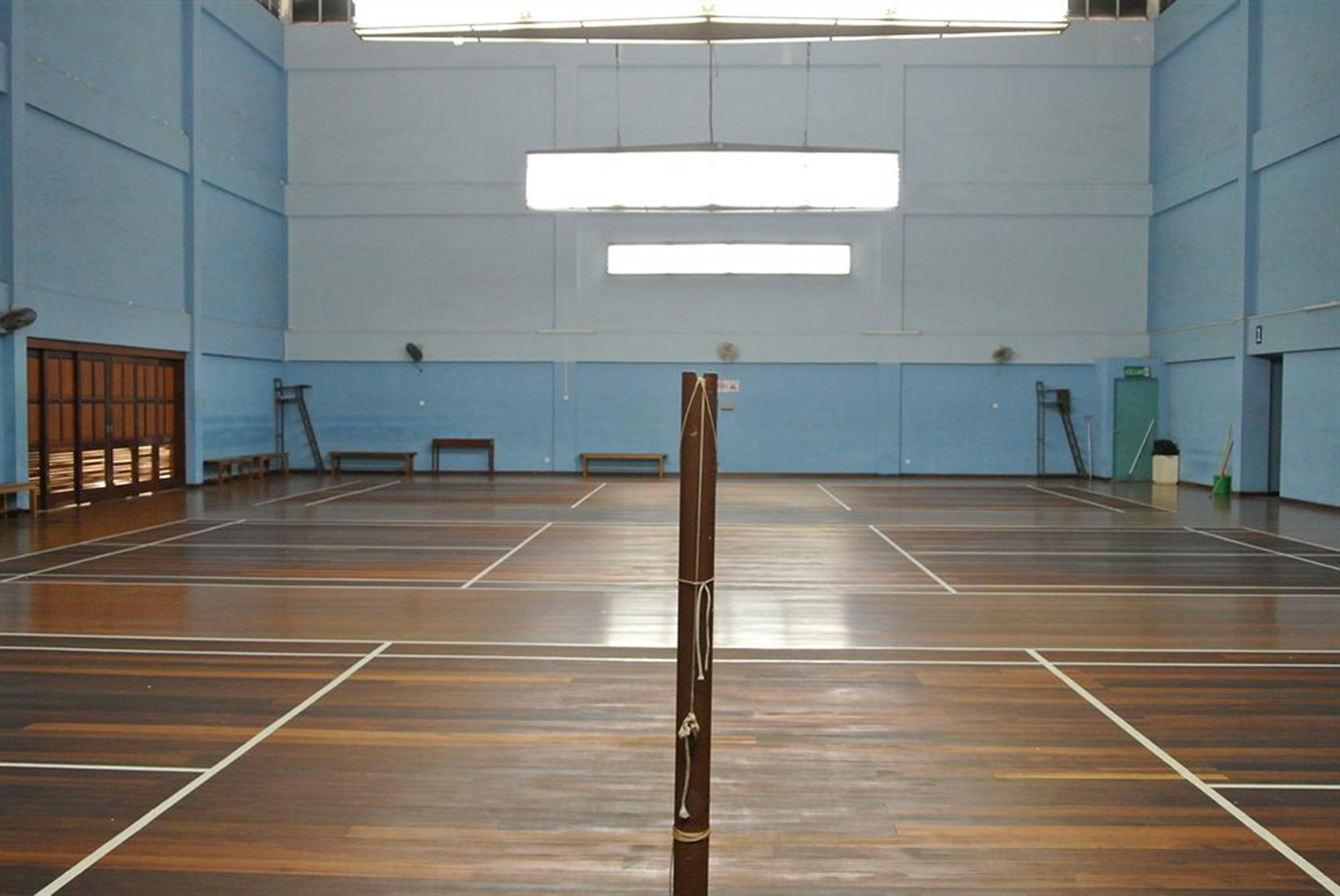An indoor sports hall with a wooden floor, benches, and a basketball hoop.