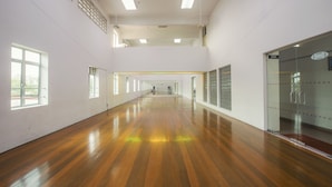 A spacious hallway with wooden flooring, large windows, and a glass elevator.