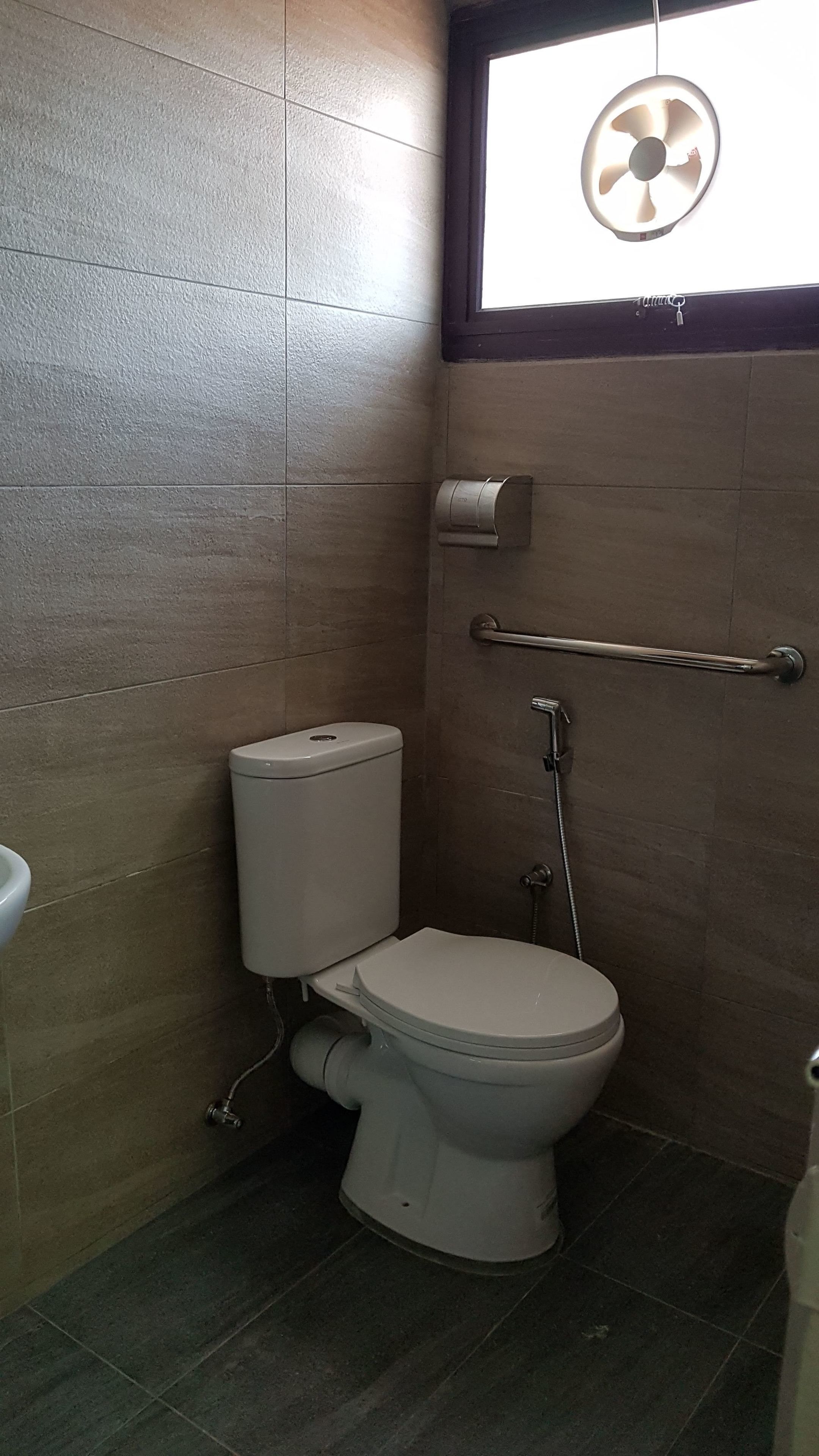 A small bathroom with a toilet, a hand dryer, and a window with a fan.