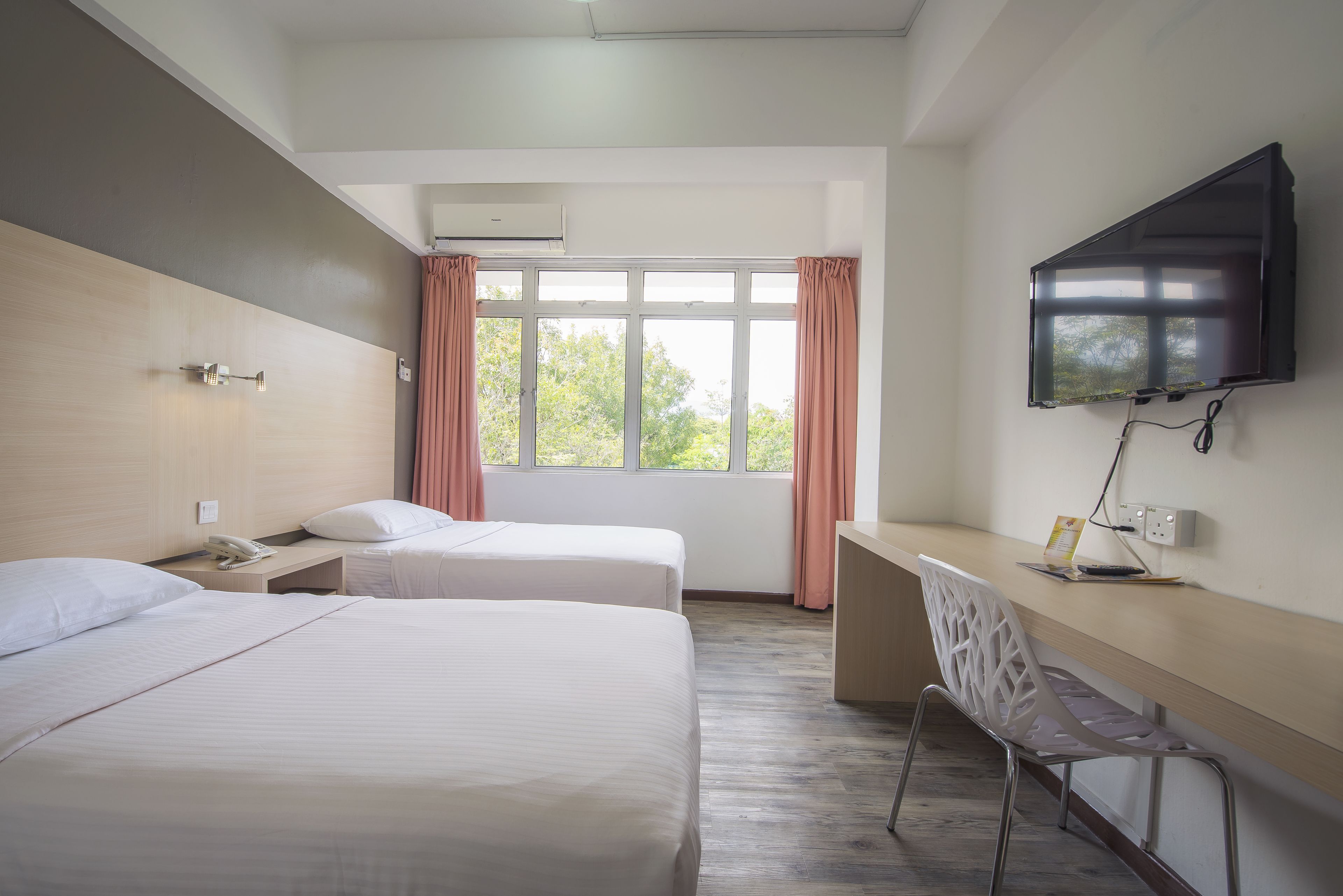 Habitación de hotel con dos camas, un escritorio, una silla, un televisor y una ventana con cortinas.