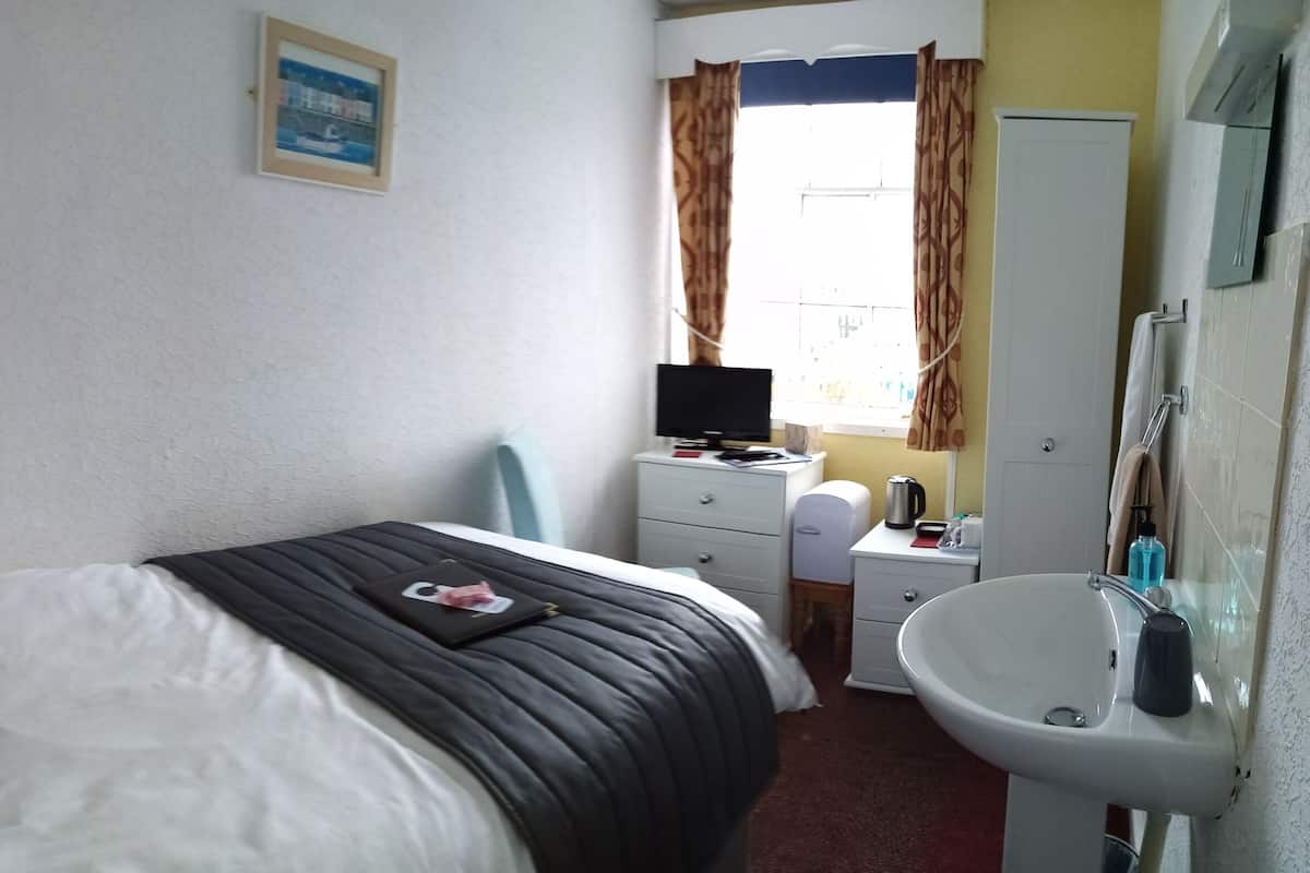 A hotel room with a bed, a desk with a computer, a sink, and a window with curtains.