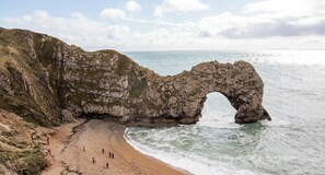 Un paysage côtier caractérisé par une arche rocheuse imposante, une plage de sable et une vue dégagée sur la mer.